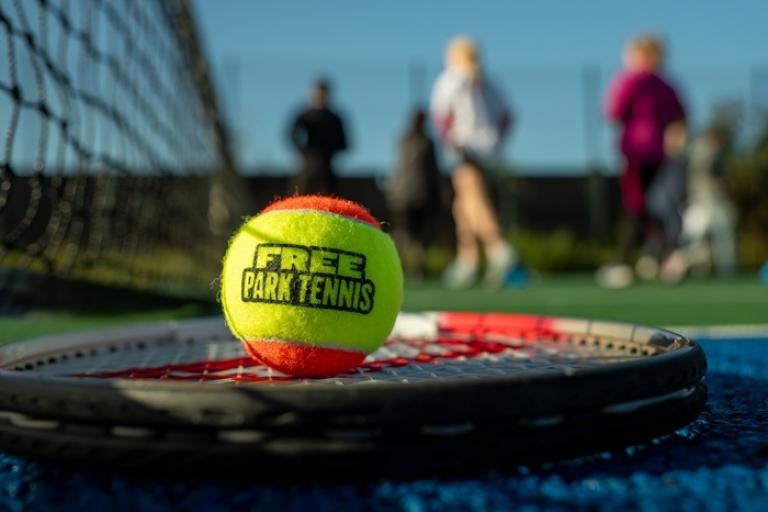 Tennis ball on a racket with the text 'Free Park Tennis' on it