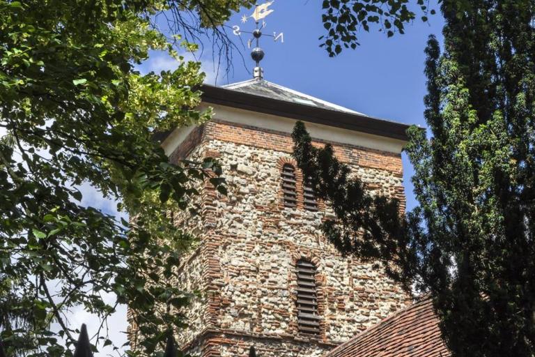 Photo of the Holy Trinity Church in Colchester surrounded by the green leaves of trees against a blue sky