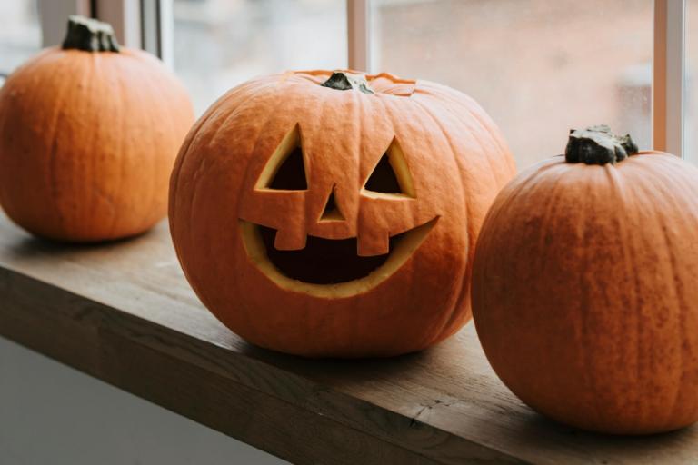 Photo of three pumpkins, the middle one has a face carved into it