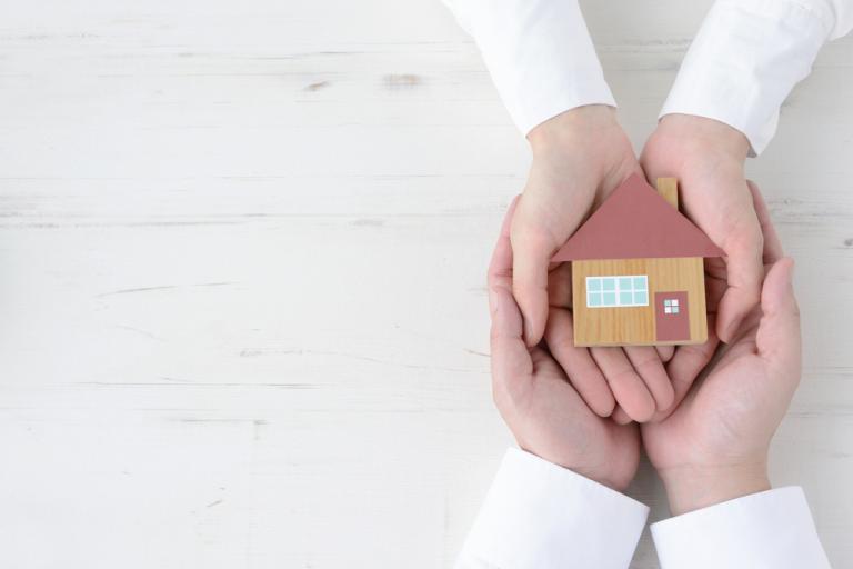 Two pairs of hands holding a model of a house