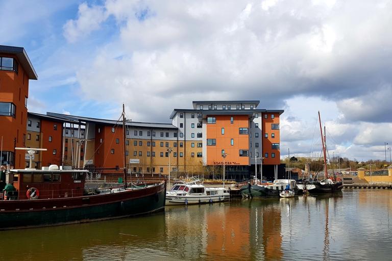 A picture of the river in Hythe Colchester with boats docked and buildings in the background