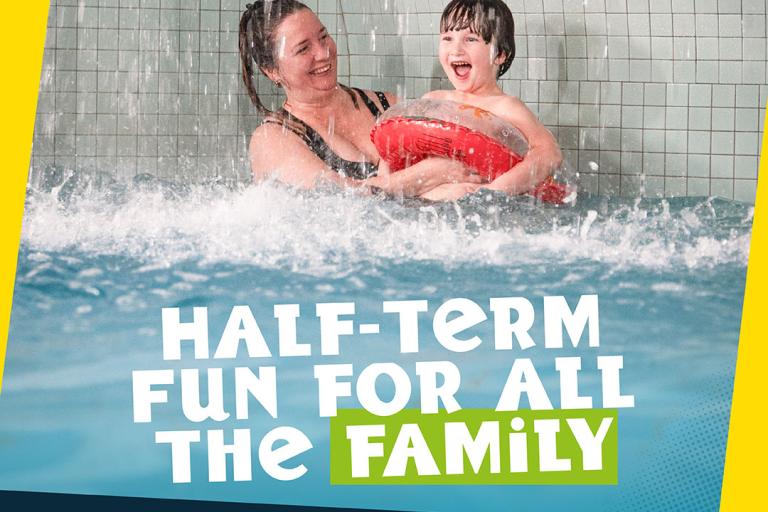 A person and a child splash together in a swimming pool, with water spraying around them as they enjoy a ride or feature in an indoor leisure pool. The image is overlaid with bold text promoting “Half-term fun for all the family,” along with branding for Colchester Sports Park and Leisure World. A banner at the bottom reads, “Family fun at all our sites!”