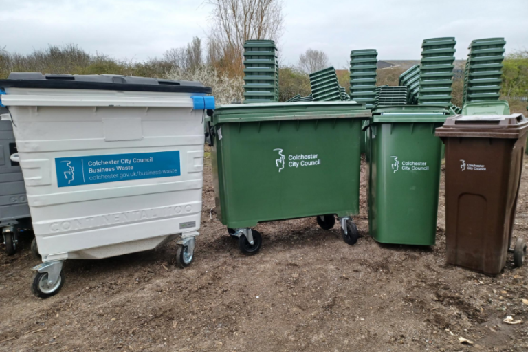 A photo of 4 business waste bins, from left to right, there is a large white bin, a large green bin, a green wheelie bin and a brown wheelie bin