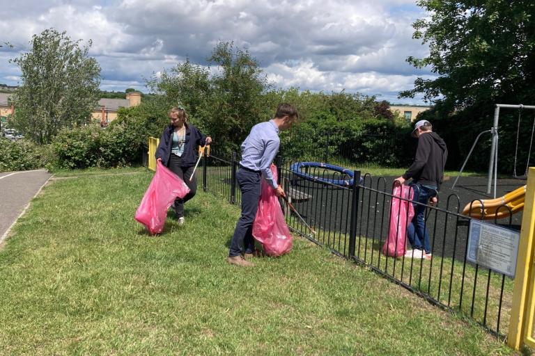 Three people with litter pickers and bags clearing up a children's playground