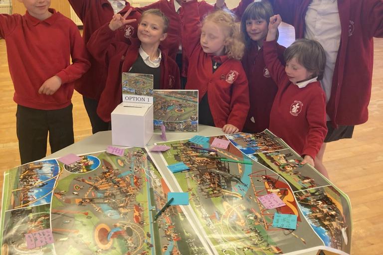 Children from Millfields Primary School stand behind large printed designs of the proposed Castle Park play area