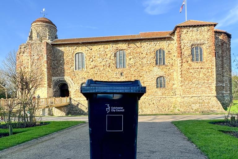 A black wheelie bin pictured with Colchester Castle in the background