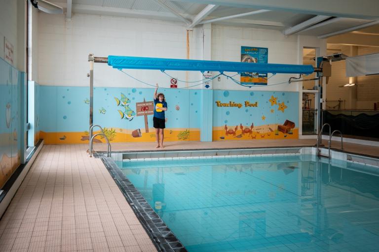 A swimming pool with a young swimmer stood poolside at one end