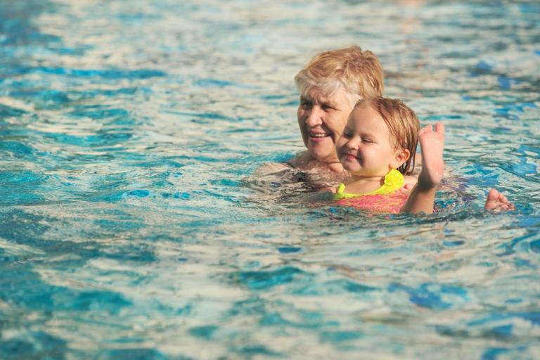 A woman holding a child above the water in a swimming pool