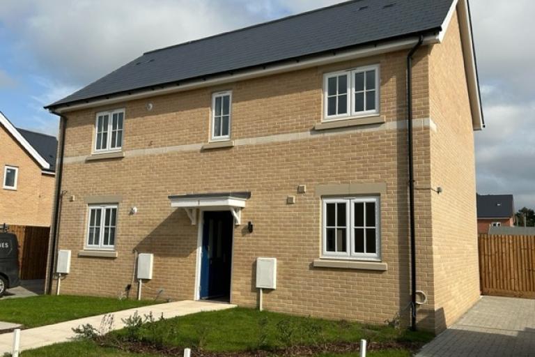 One of the new council-build homes at Chesterwell. A modern two‑storey detached brick house with a dark roof, white-framed windows, and a small front garden beside a paved path.