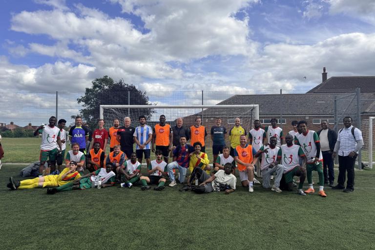 A large group of people pose on a football pitch in front of a goal.