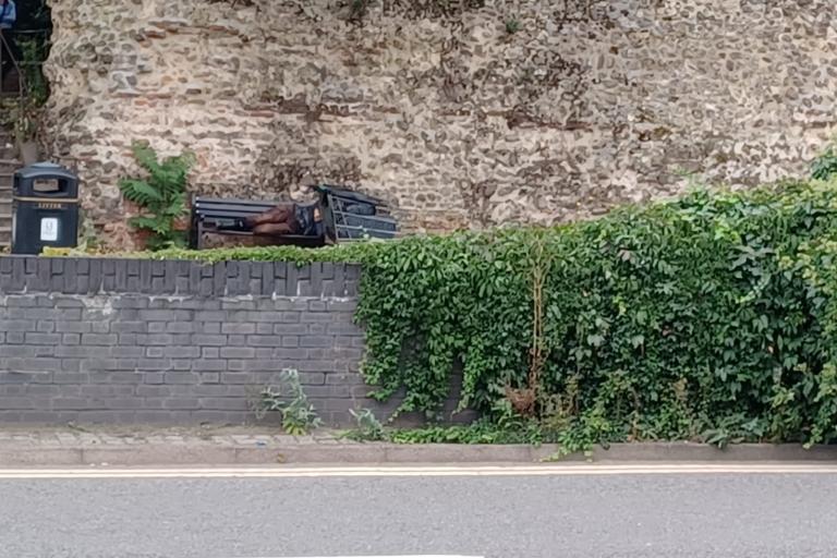 A person sleeping on a bench beneath Colchester's Roman Wall