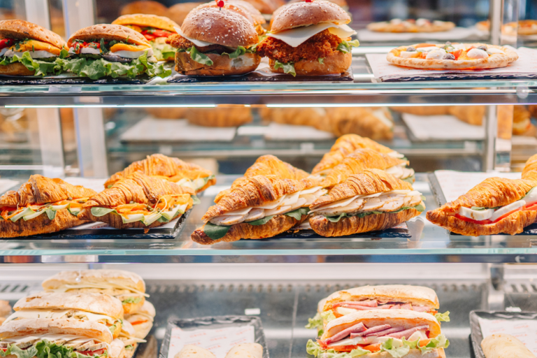 Assorted sandwiches, croissants, burgers and a pizza displayed in a refrigerated café cabinet