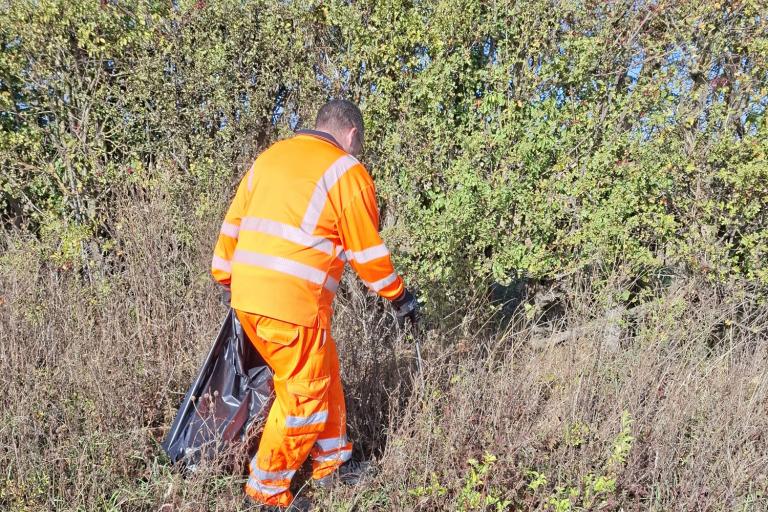 An operative wearing high-visibility clothing clearing litter from a hedge