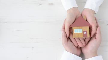 Two pairs of hands holding a model of a house