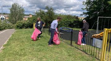 Three people with litter pickers and bags clearing up a children's playground