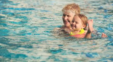 A woman holding a child above the water in a swimming pool