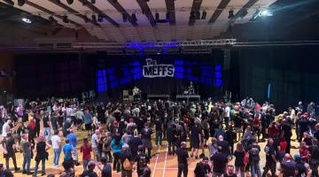 A large crowd stands inside Charter Hall facing a stage with “The Meffs” backdrop.