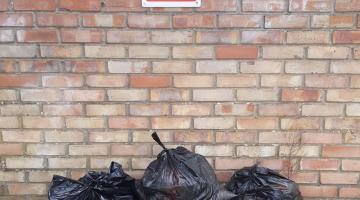 Three dumped black bags in front of a brick wall with a sign saying "No Fly Tipping"