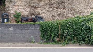 A person sleeping on a bench beneath Colchester's Roman Wall