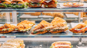 Assorted sandwiches, croissants, burgers and a pizza displayed in a refrigerated café cabinet