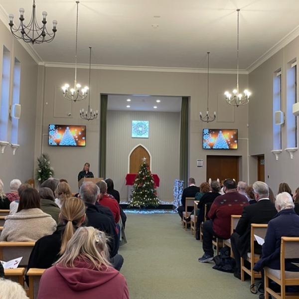 Photo of the inside of the crematorium, people are sitting in rows of chairs.