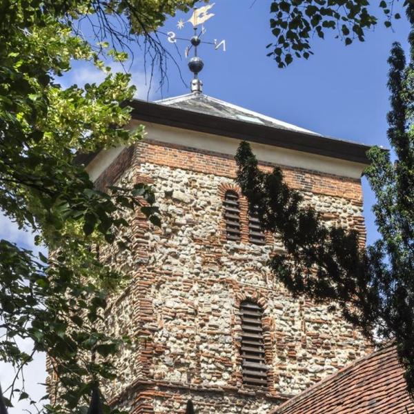Photo of the Holy Trinity Church in Colchester surrounded by the green leaves of trees against a blue sky
