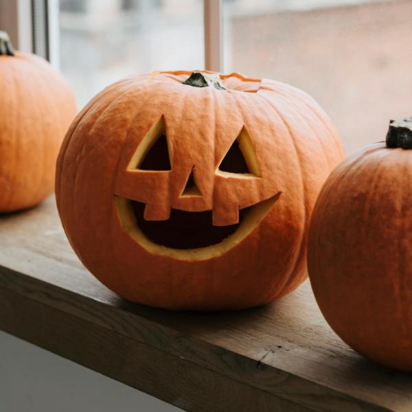 Photo of three pumpkins, the middle one has a face carved into it