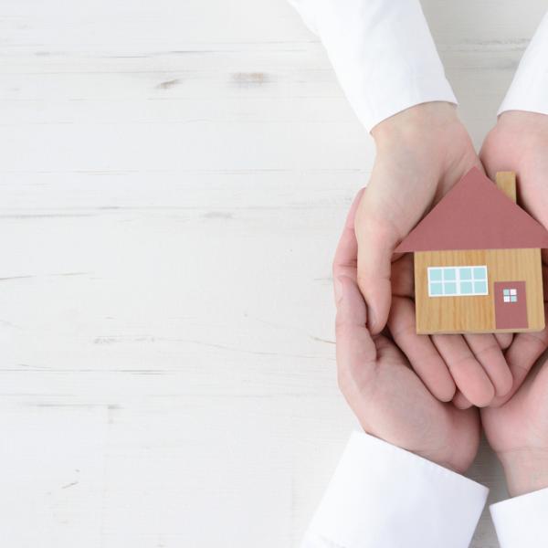 Two pairs of hands holding a model of a house