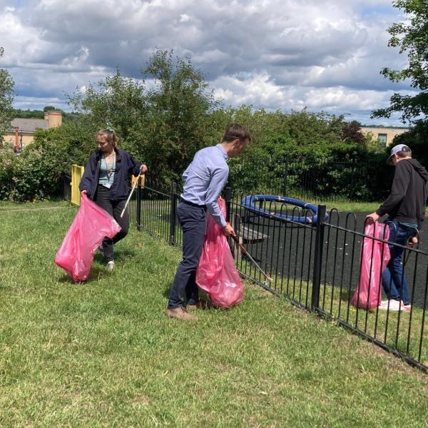 Three people with litter pickers and bags clearing up a children's playground
