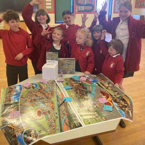 Children from Millfields Primary School stand behind large printed designs of the proposed Castle Park play area