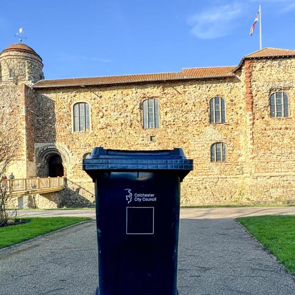 A black wheelie bin pictured with Colchester Castle in the background