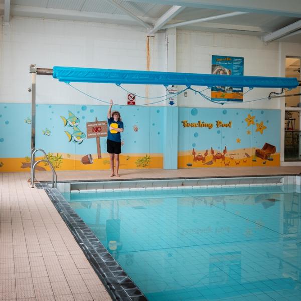 A swimming pool with a young swimmer stood poolside at one end