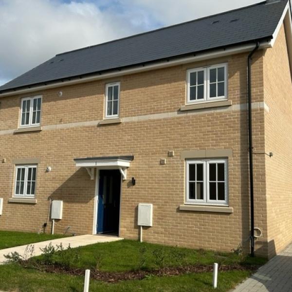 One of the new council-build homes at Chesterwell. A modern two‑storey detached brick house with a dark roof, white-framed windows, and a small front garden beside a paved path.