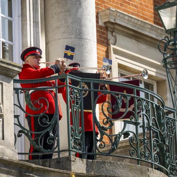 Two soldiers in red uniforms play trumpets on the decorative balcony of Colchester Town Hall