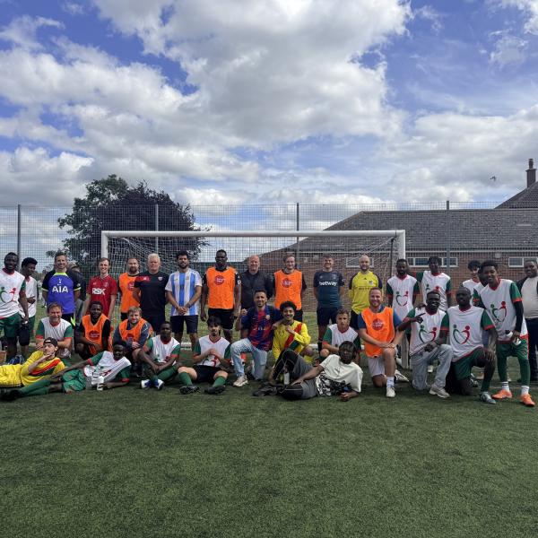 A large group of people pose on a football pitch in front of a goal.