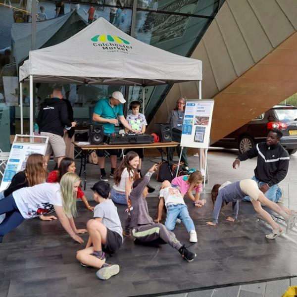 People on a dance mat beneath a market stall canopy outside a modern building