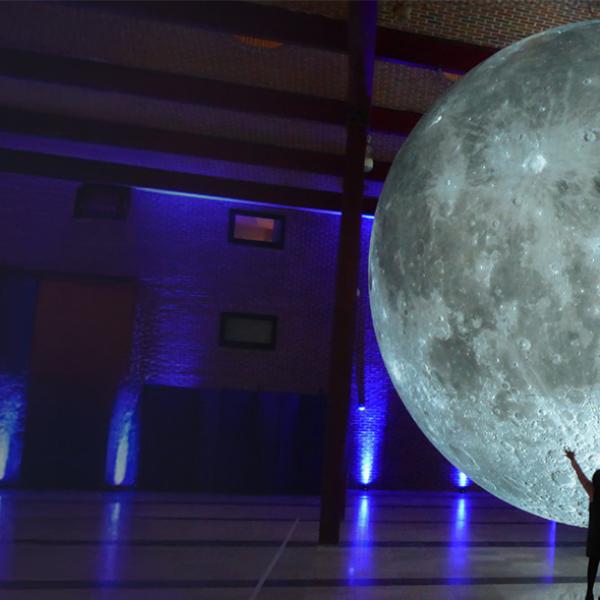 Large glowing moon in a hall and people standing beside it.