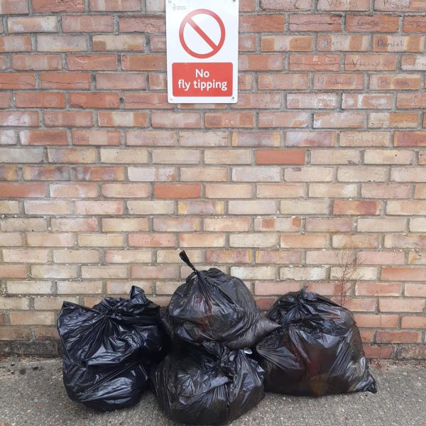 Three dumped black bags in front of a brick wall with a sign saying "No Fly Tipping"