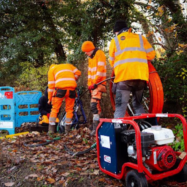 A group of people in high-visibility clothing working beside a roadside cable installation with equipment and orange ducting.